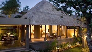 A modern villa with a thatched roof, a pool area, and a well-lit outdoor seating space.