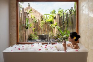 Una bañera con vista a una cerca de bambú y plantas tropicales.