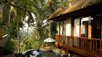 A pool area with a wooden deck and a thatched roof structure, surrounded by lush greenery.