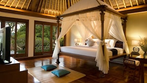 A four-poster bed with a canopy, a television, and a desk with a chair in a room with wooden flooring and large windows.