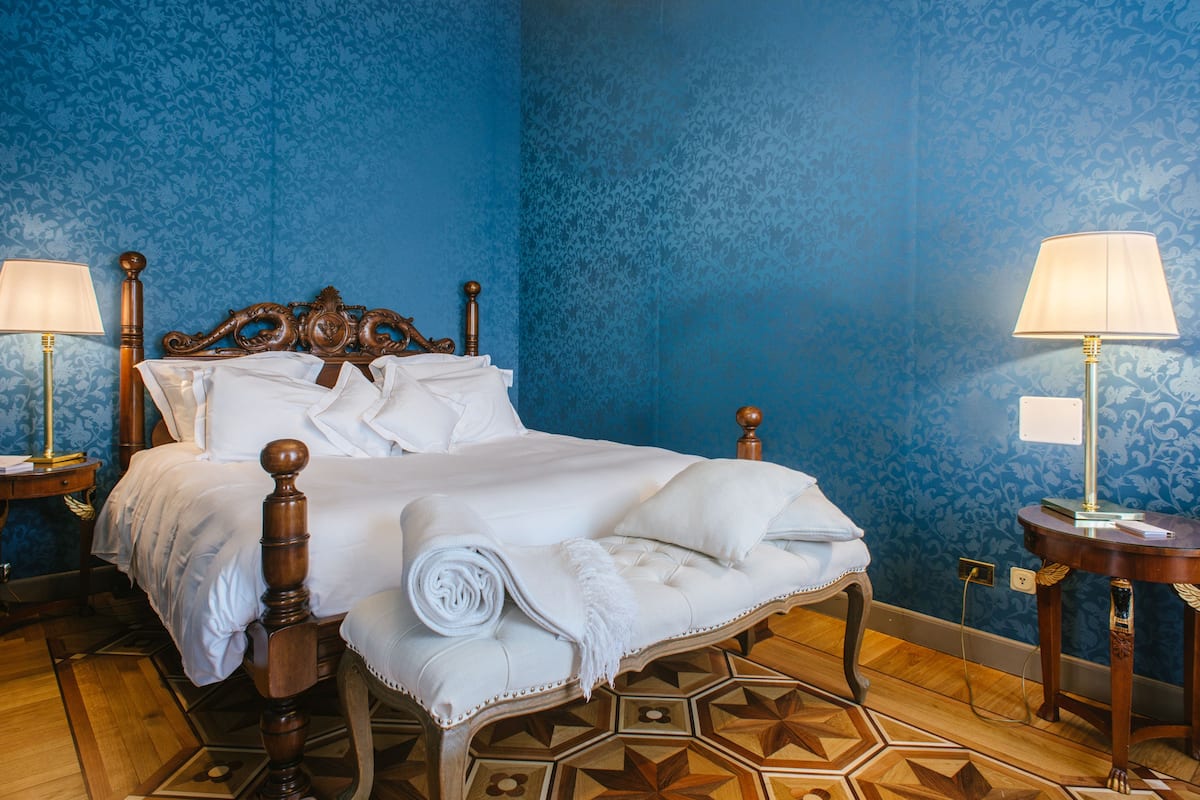 Una cama bien hecha con sábanas blancas, cabecera de madera y suelo con estampado geométrico.