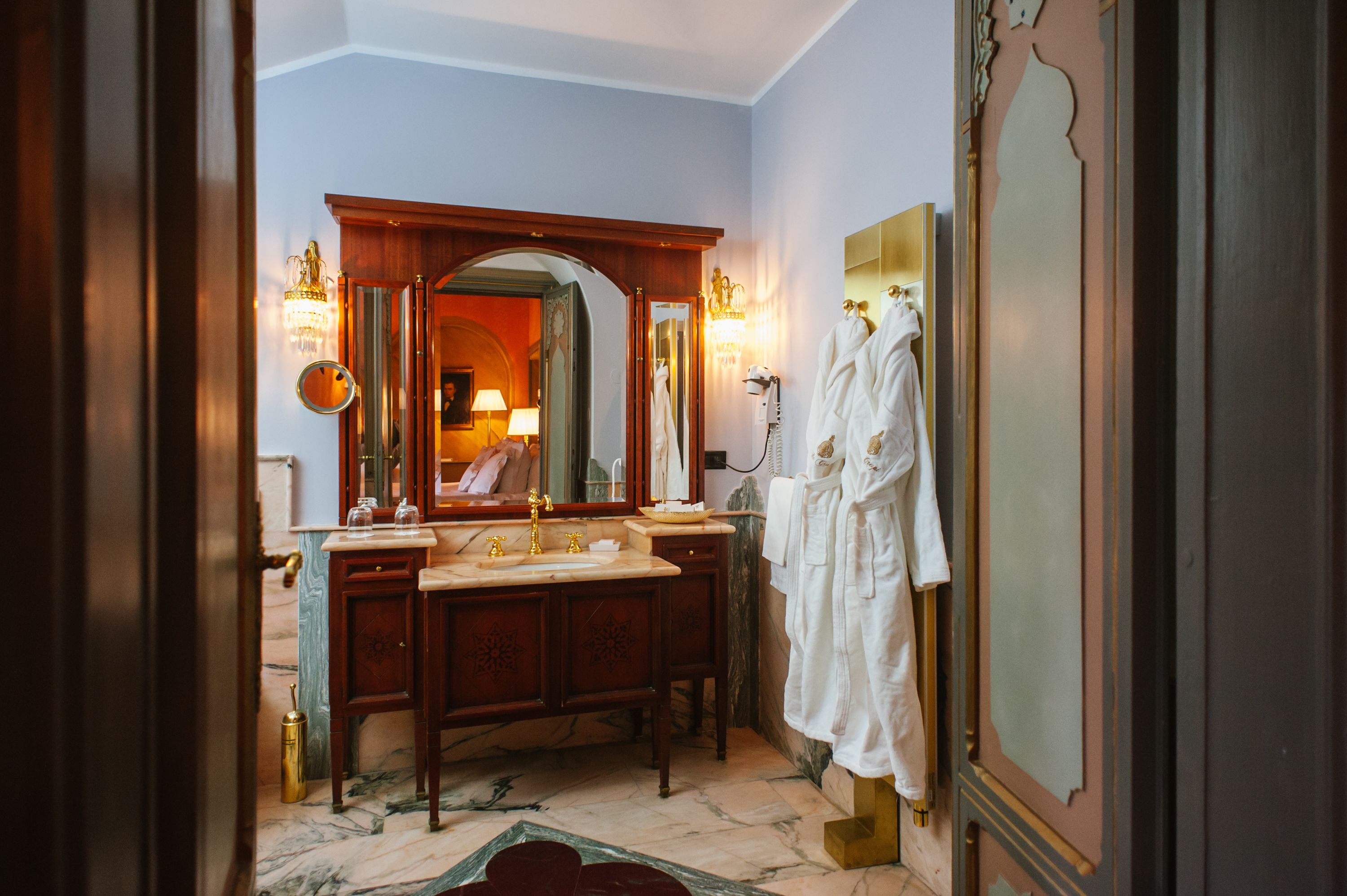 Un baño con un espejo grande, tocador y dos albornoces blancos colgados en una pared.