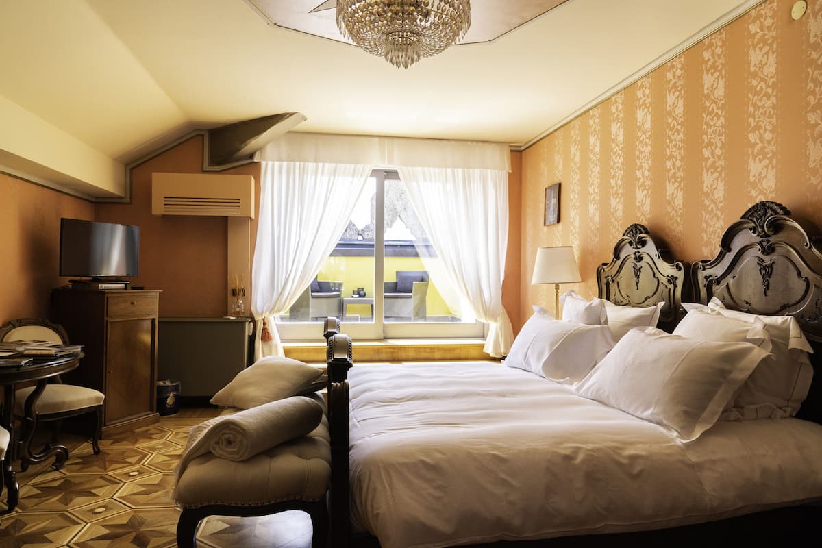 Habitación de hotel con una cama grande, un escritorio con televisor, una silla y una ventana con cortinas.