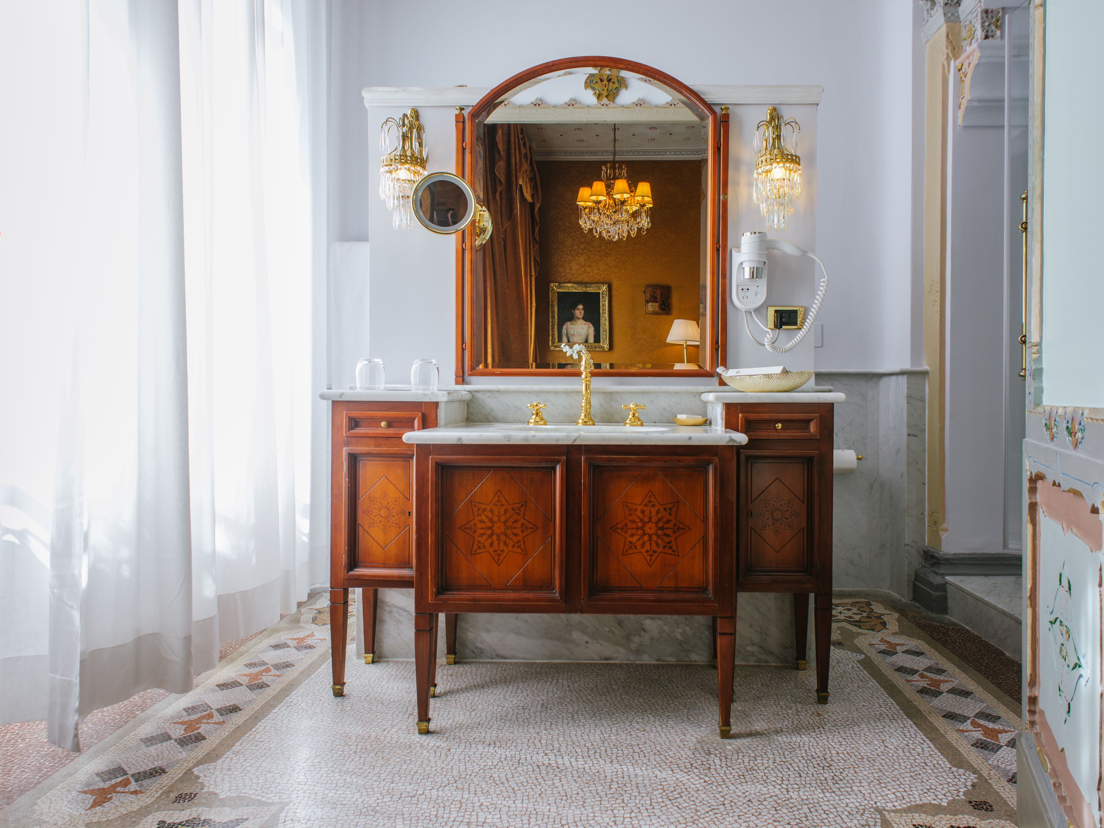 A classic bathroom with a marble sink, ornate wooden cabinetry, and a large mirror.