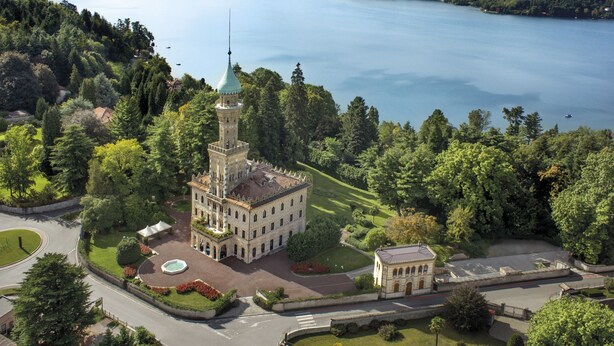 An aerial view of a historic building with a tower, surrounded by lush greenery and a lake.