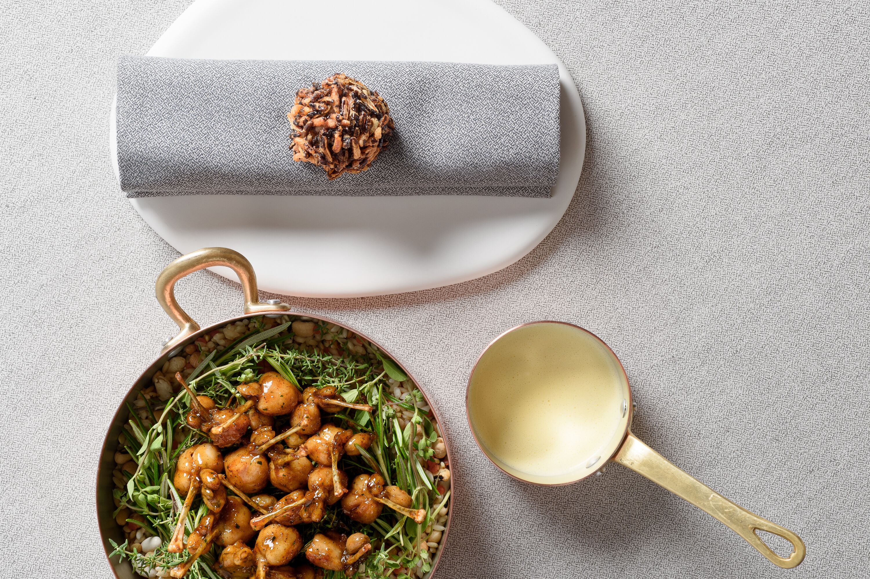 Una ciotola di pollo cotto con erbe aromatiche, una mestola dorata e una scatola grigia a trama, con una noce sopra.