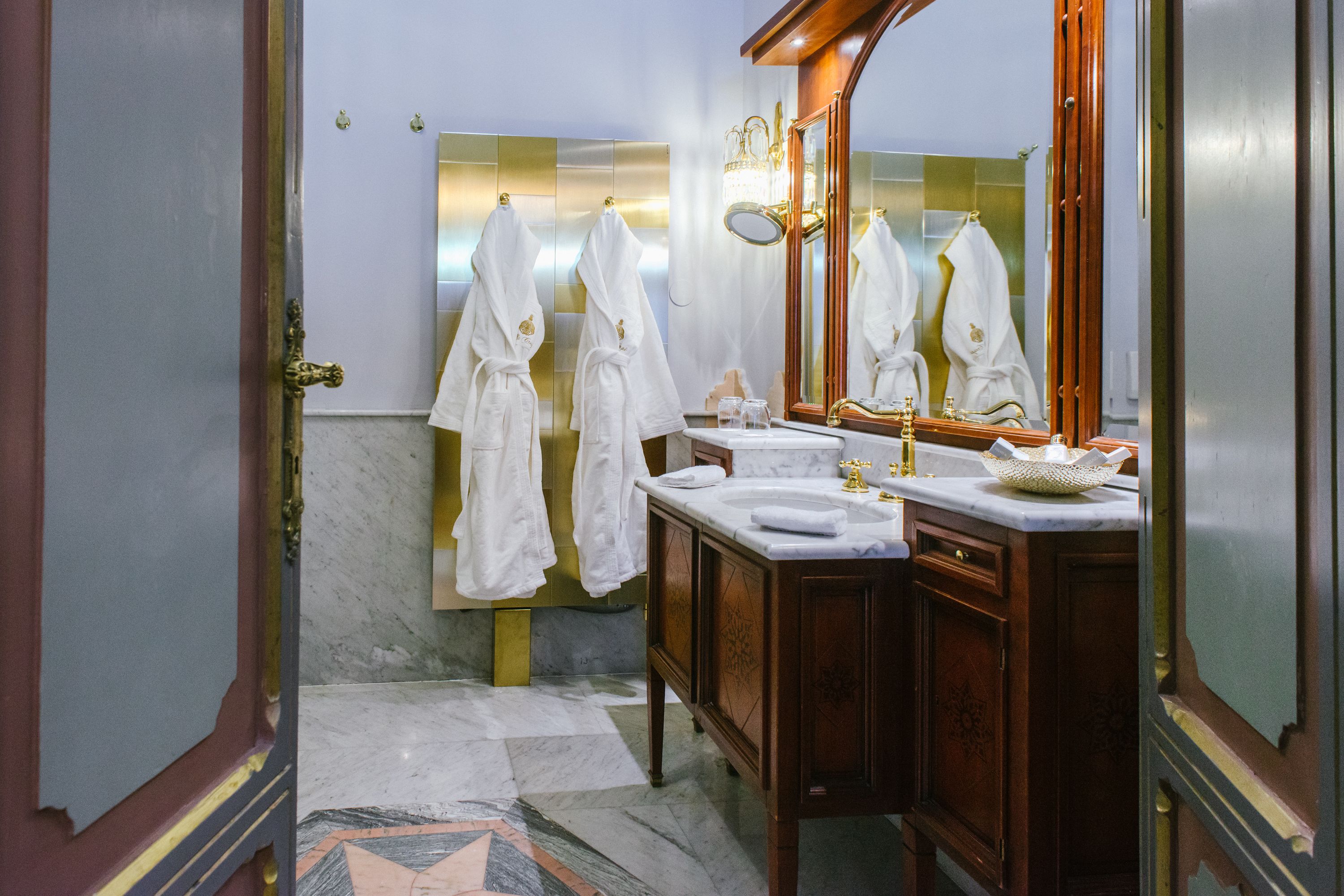 A bathroom with marble floors, a wooden vanity, a large mirror, and white towels hanging on the wall.
