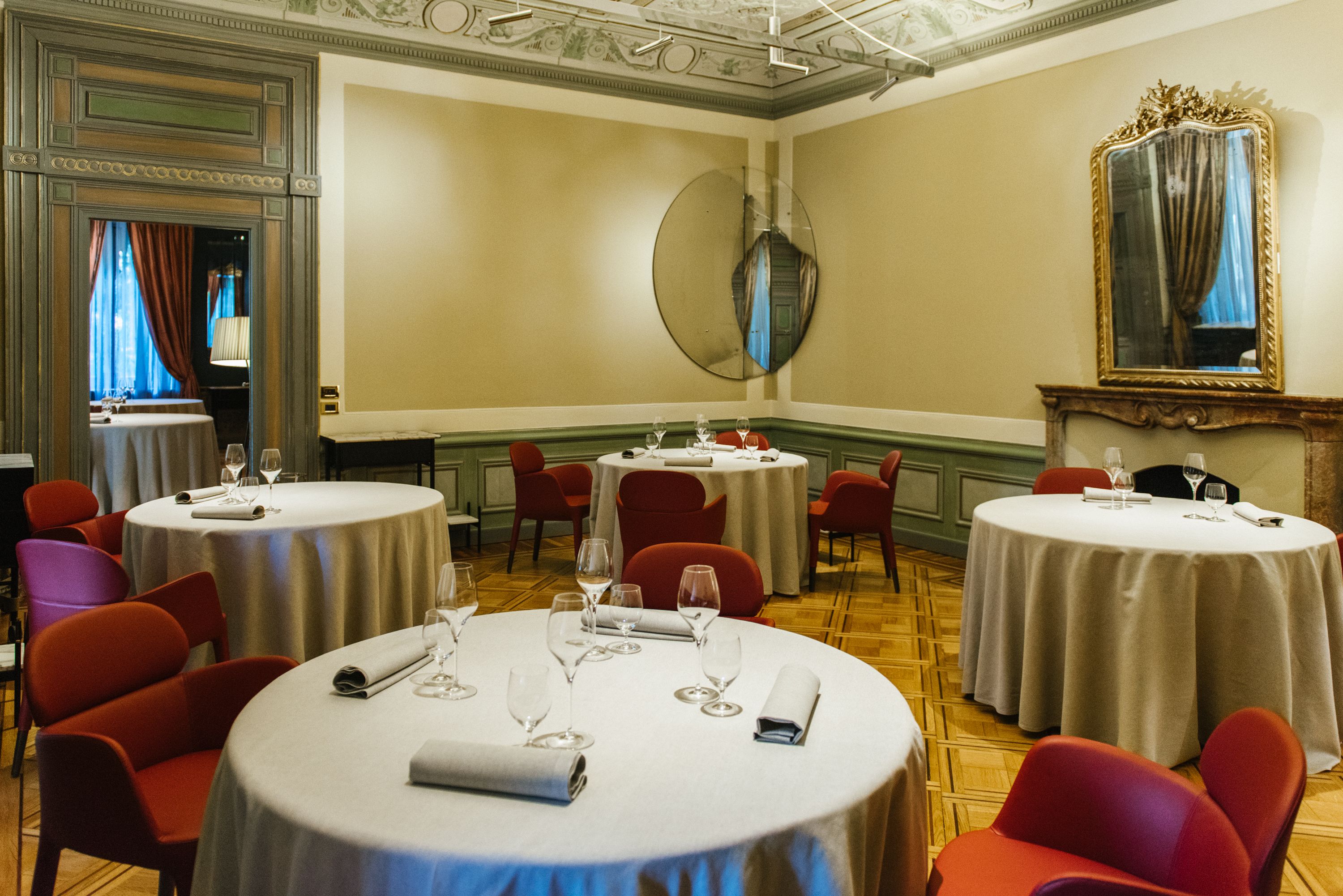 Un comedor con mesas redondas, sillas rojas y manteles blancos.