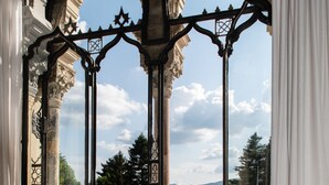 A room with ornate window frames and a view of a lake surrounded by trees and mountains.