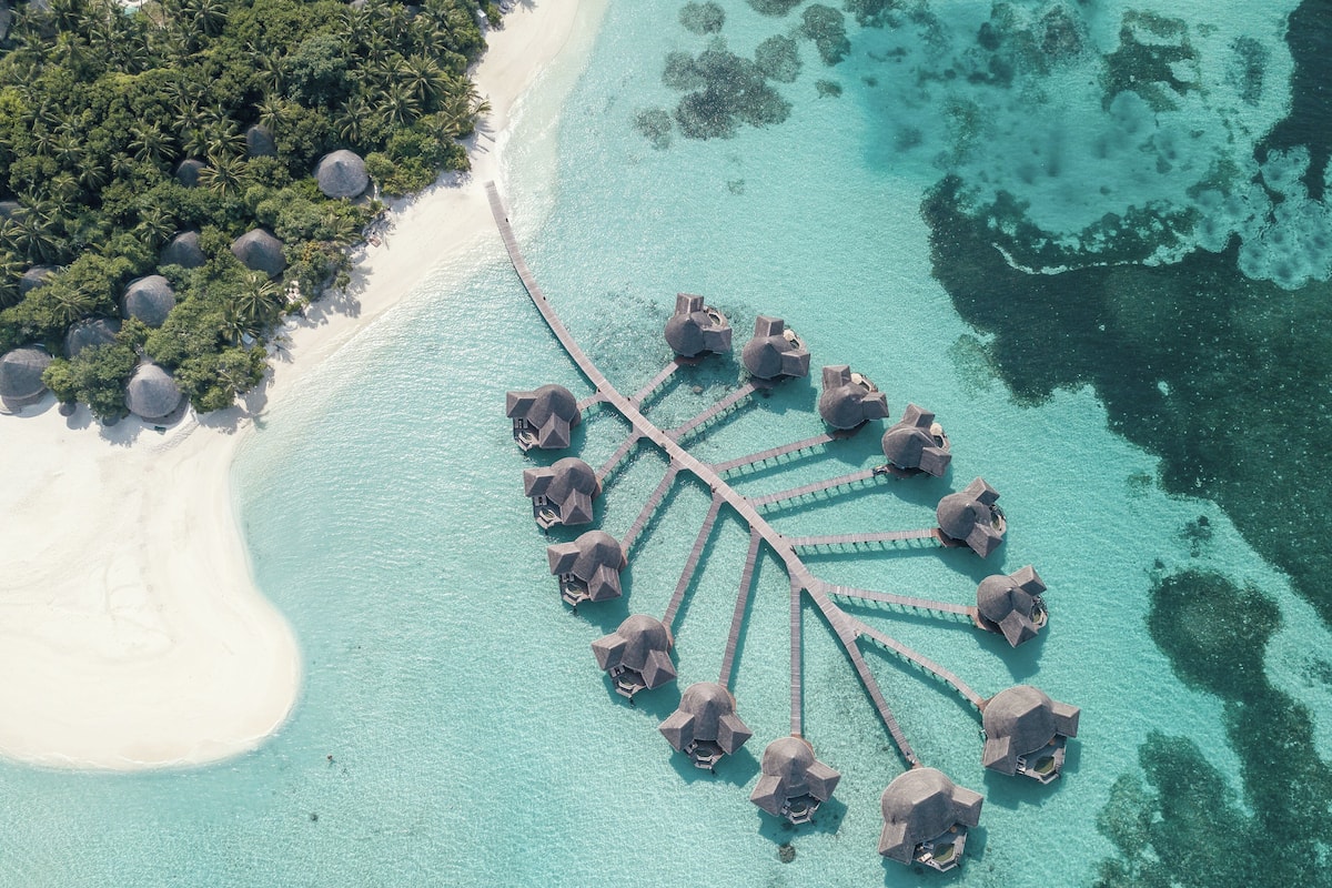 An aerial view of a resort with overwater bungalows connected by a wooden walkway.