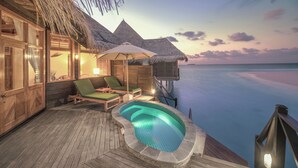 Une terrasse en bois avec une piscine, des chaises longues et une structure surmontée d’un toit de chaume.