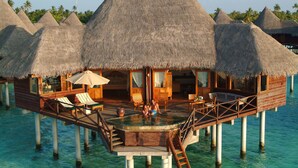 Des bungalows sur pilotis dotés de toits de chaume, de terrasses en bois et d’un espace piscine central.