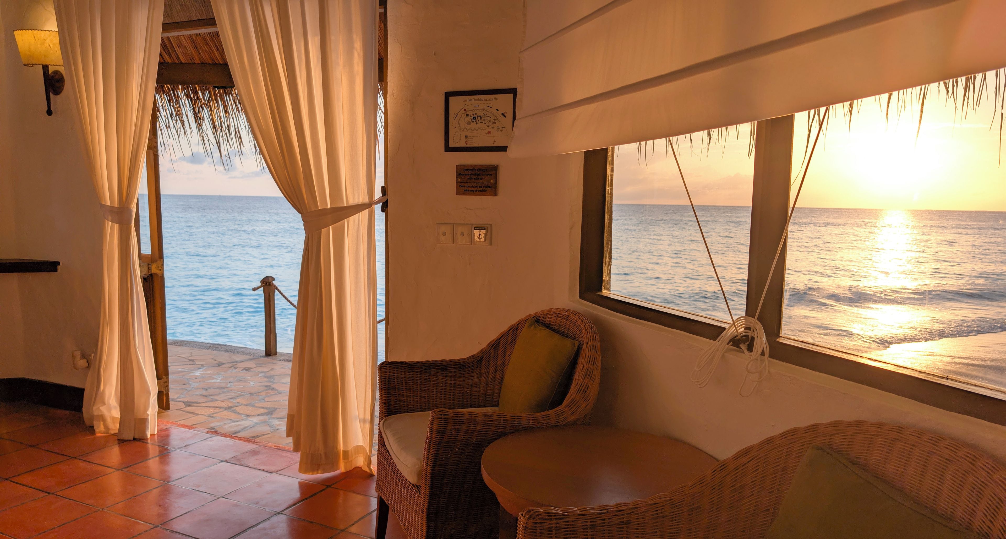A room with a view of the sea, a wicker chair, a table, and a curtain.