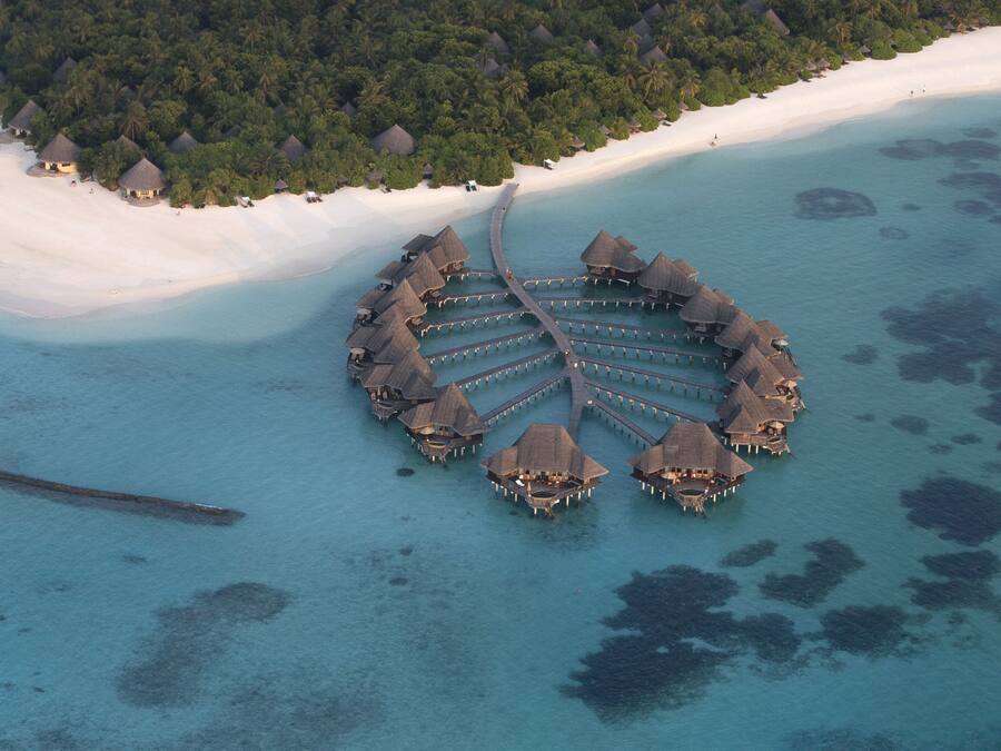 An overwater bungalows structure with a central walkway, surrounded by clear turquoise waters and a white sandy beach.