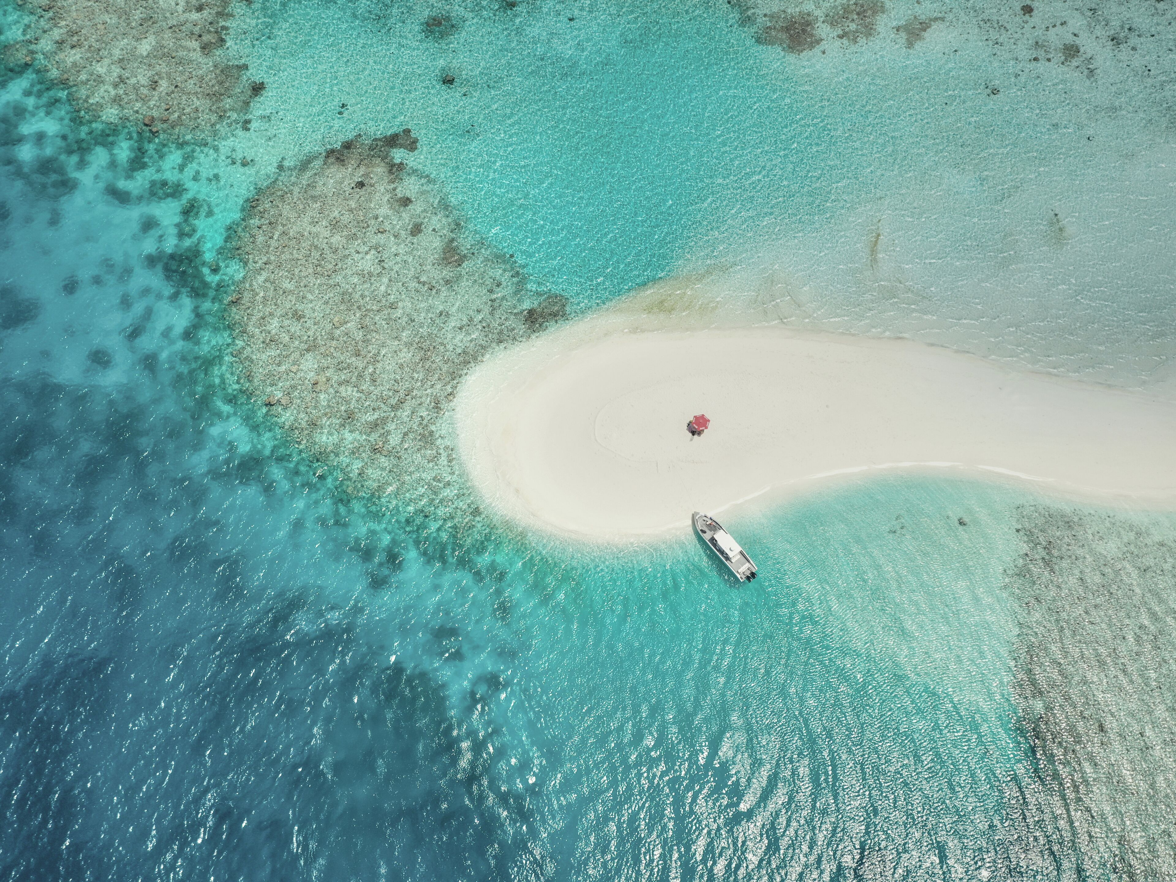 Vista aérea de una playa con aguas turquesas cristalinas, una extensión de arena blanca y un bote.