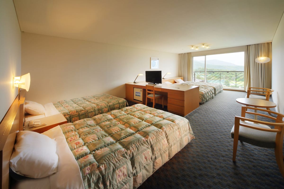 A hotel room with two beds, a desk with a computer, a chair, and a view of the mountains.