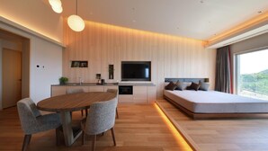 A modern bedroom with a large bed, a TV, and a dining area with a table and chairs.
