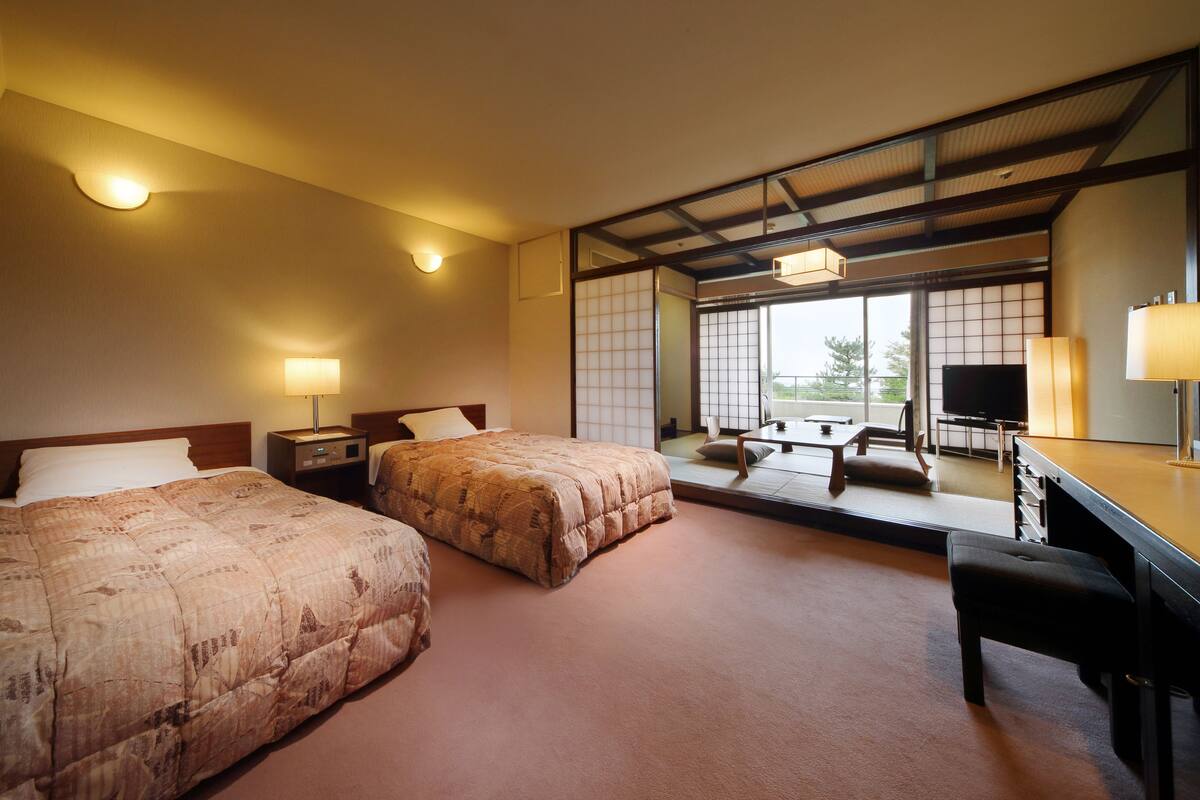 A hotel room with two beds, a desk, a chair, and a TV.