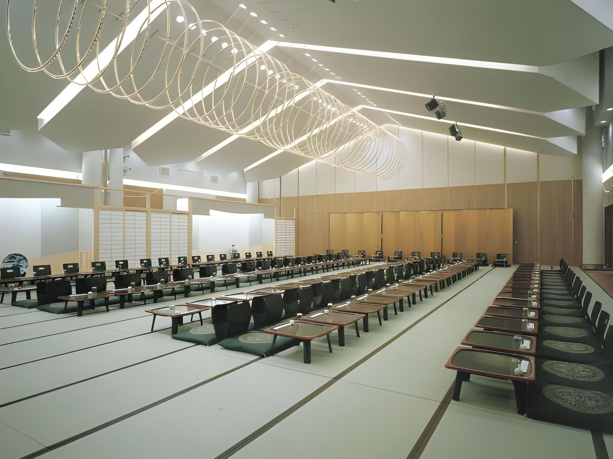 A conference room with long tables and chairs, a modern ceiling design, and a large wooden panel wall.