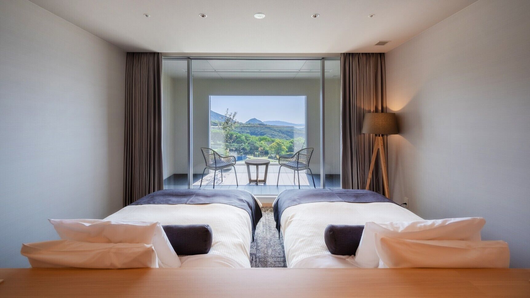 Une chambre avec deux lits, un balcon avec une table et des chaises, et une vue sur l’extérieur.