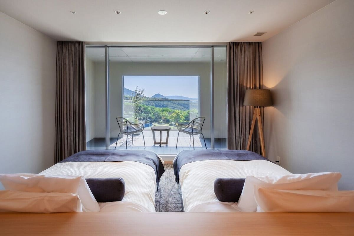 A bedroom with two beds, a balcony with a table and chairs, and a view of the outdoors.