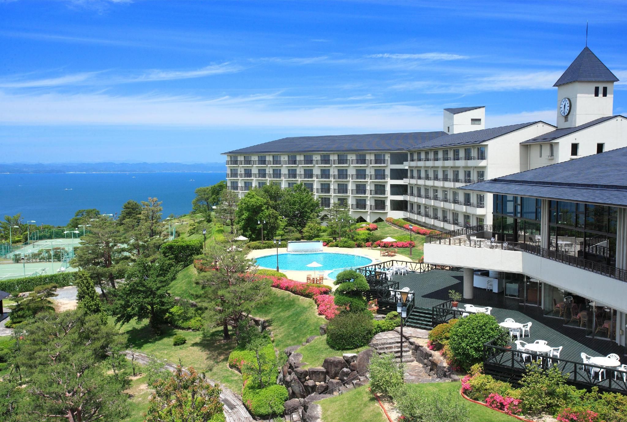 A hotel with a swimming pool, lush greenery, and a view of the sea.