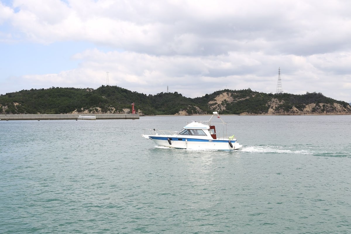 A small boat on calm water with a hilly landscape in the background.