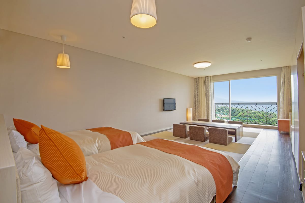 A hotel room with two beds, a small seating area, a TV, and a balcony with a view.