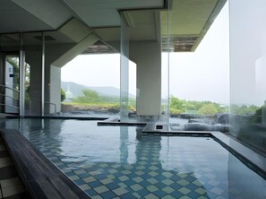 An indoor swimming pool with clear glass walls, a tiled floor, and a view of greenery and mountains in the background.