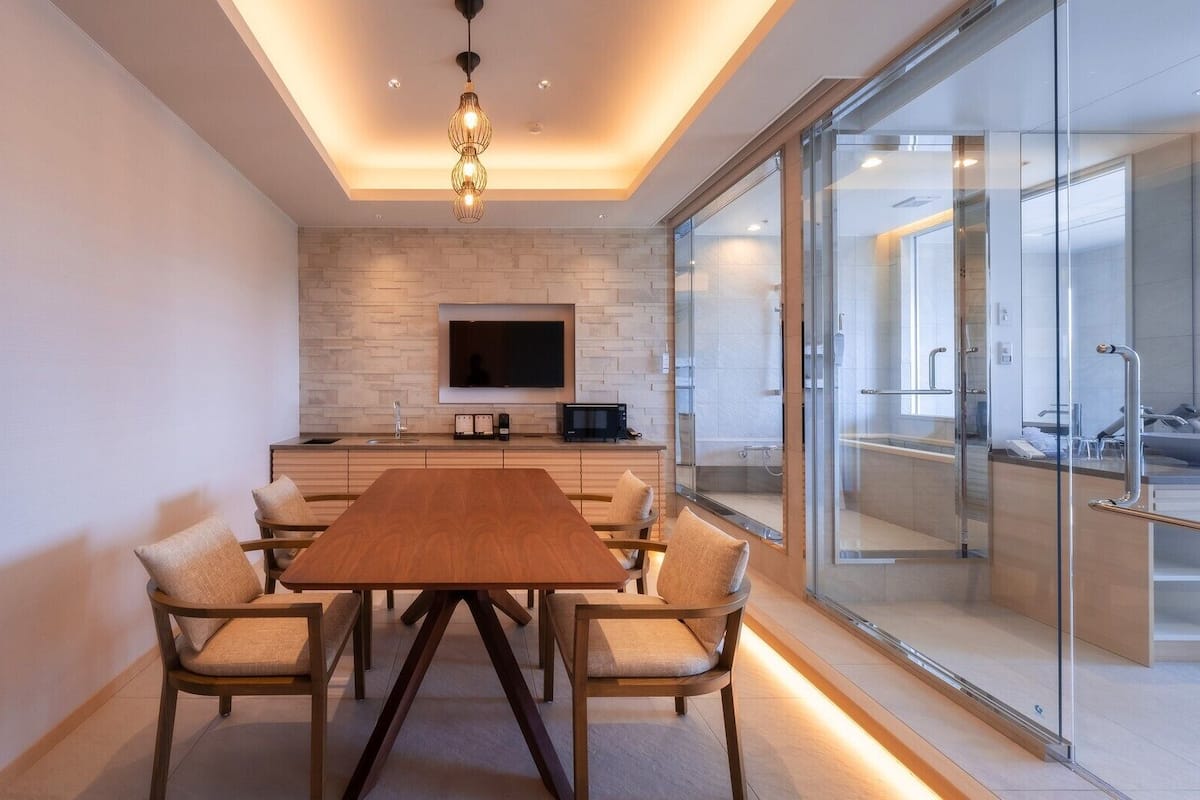 A modern kitchen with a TV, a dining table with chairs, and a glass shower area.