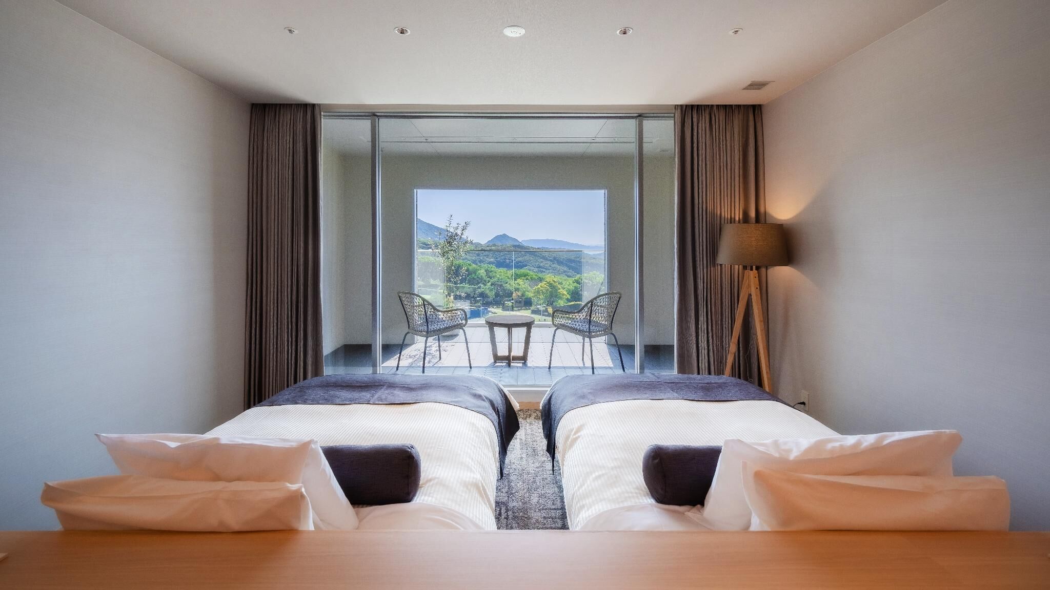 Habitación de hotel con dos camas, un balcón con mesa y sillas, y vistas al exterior.