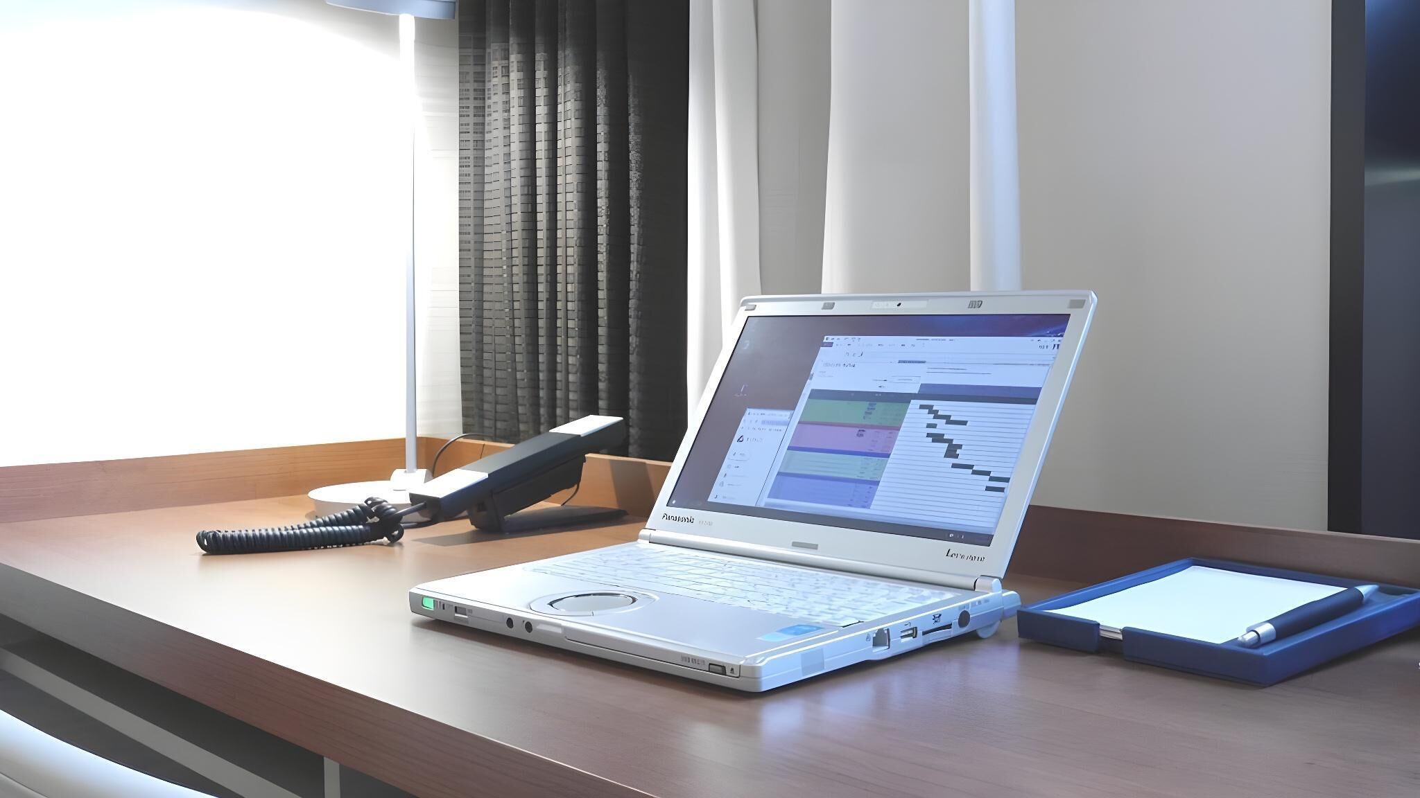 A laptop on a desk with a phone and a tablet.