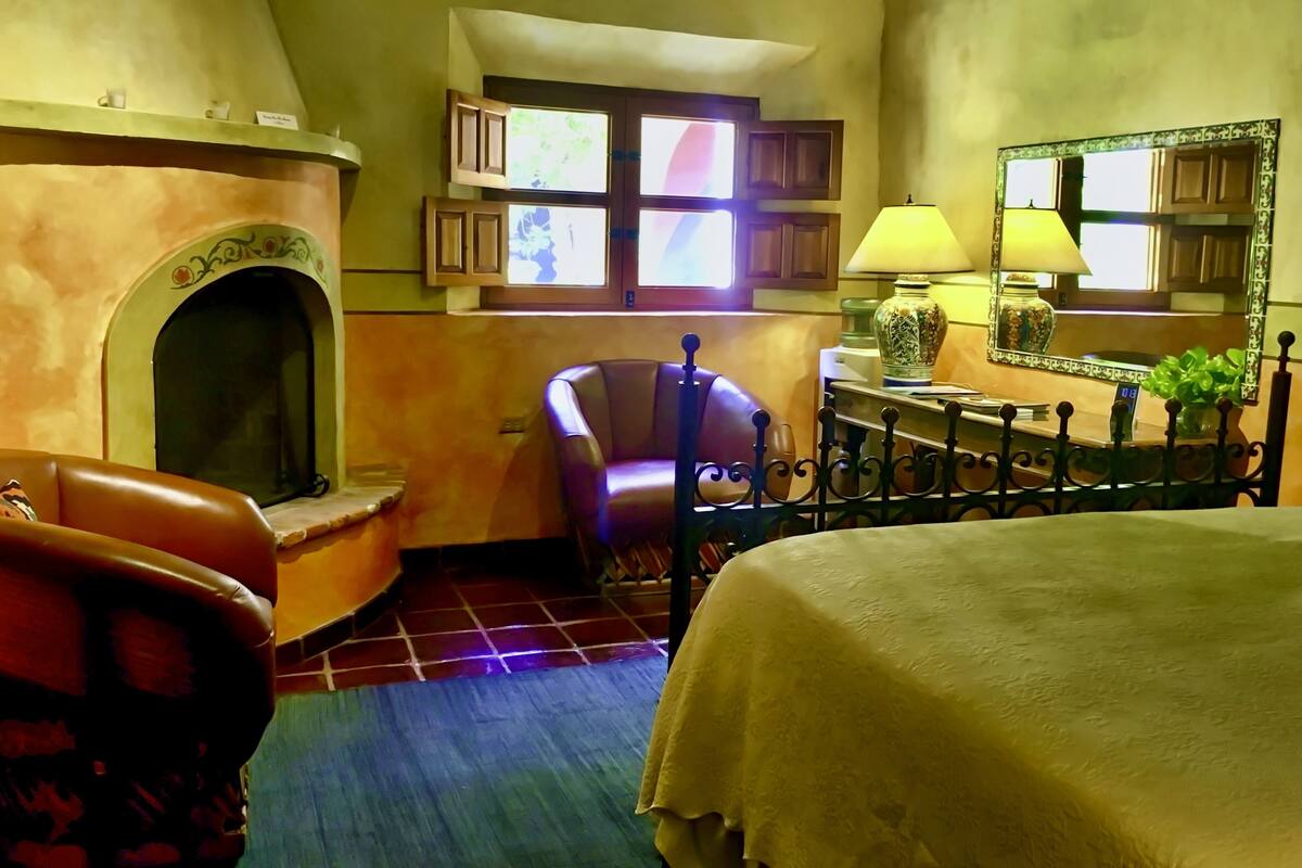 A cozy room with a fireplace, a leather armchair, a bed, and a table with a lamp.