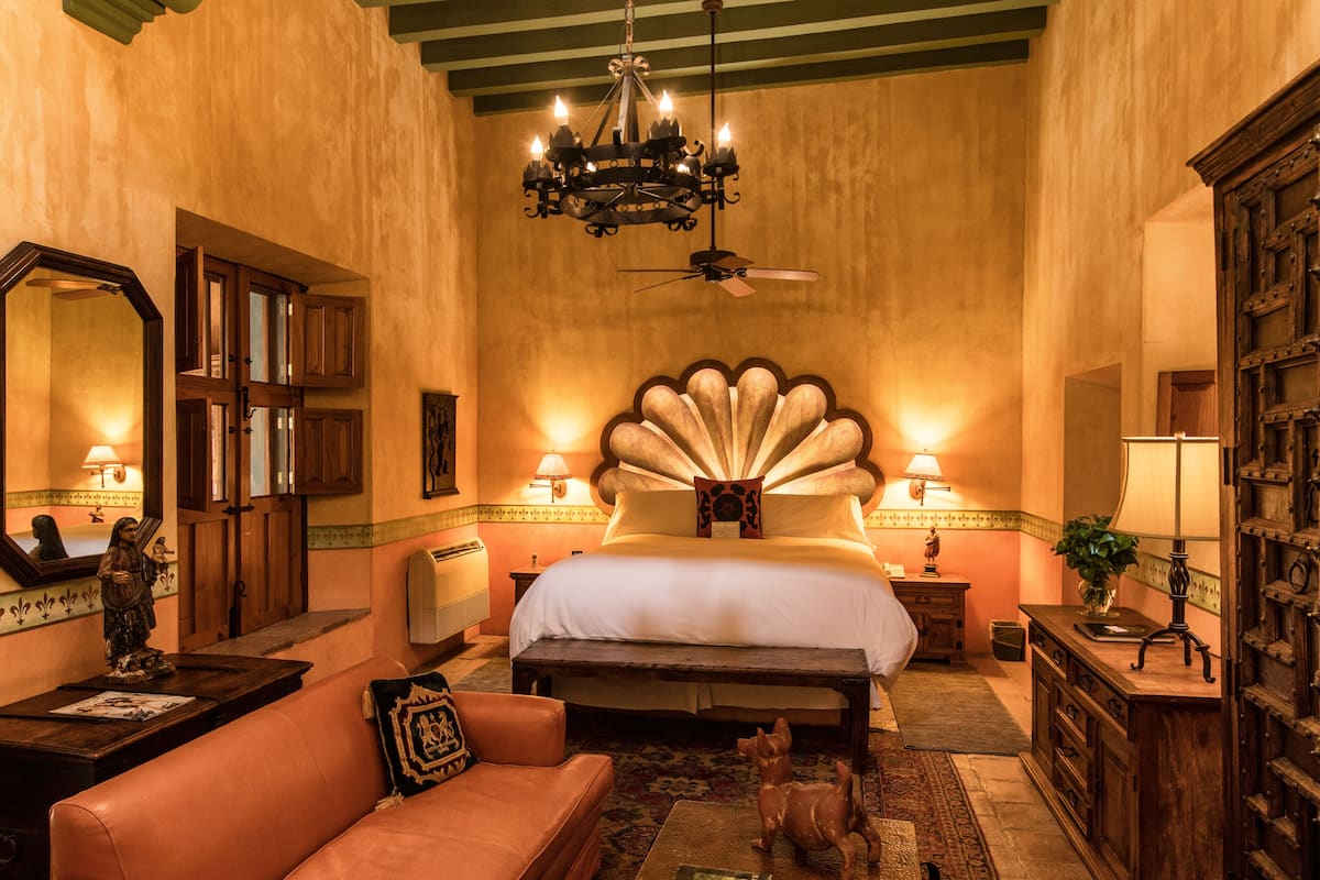 A bedroom with a large bed, a ceiling fan, a chandelier, and a wooden dresser.