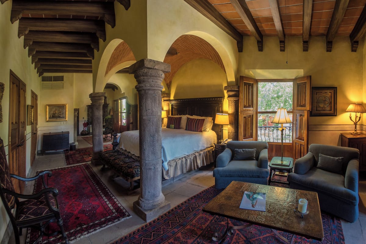 A spacious hotel room with a large bed, two armchairs, a coffee table, and a fireplace.