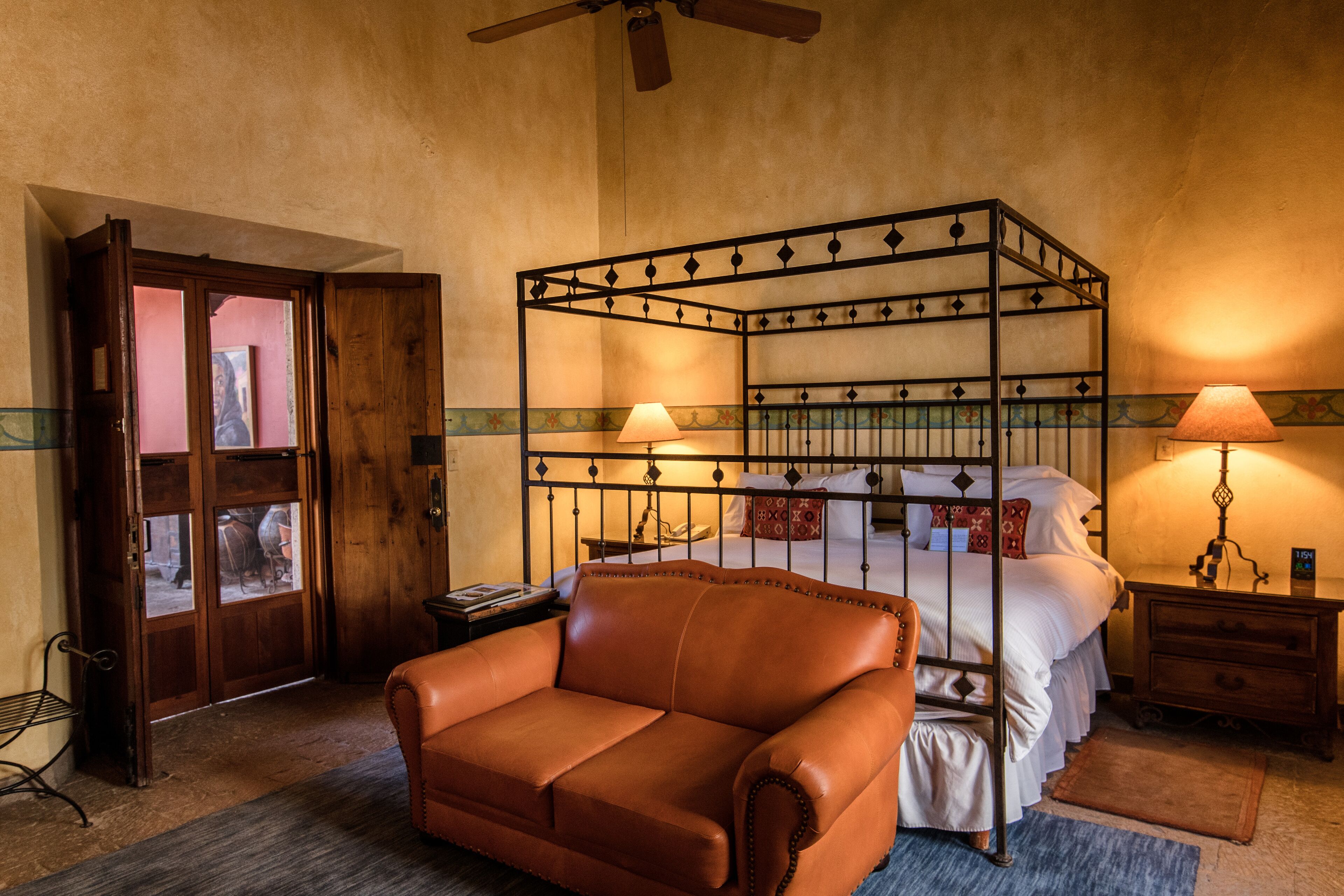 A bedroom with a four-poster bed, a leather armchair, and a wooden door.
