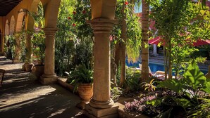 An outdoor patio area with arches, potted plants, and a pool in the background. - Hacienda de los Santos (Alamos)