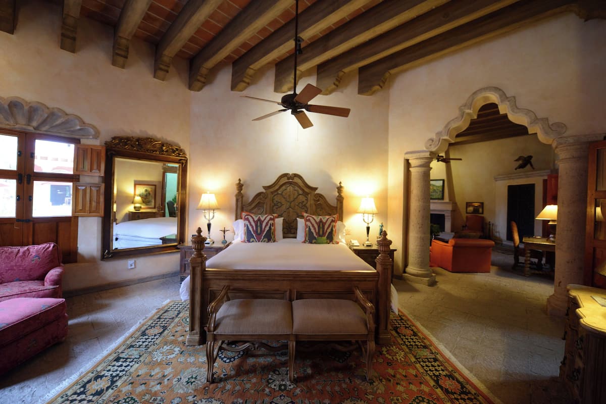 A bedroom with a large bed, a ceiling fan, a mirror, and a pink chair.