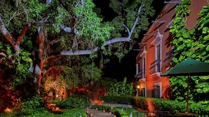 A nighttime garden pathway leading to a building with a balcony. - Hacienda de los Santos (Alamos)
