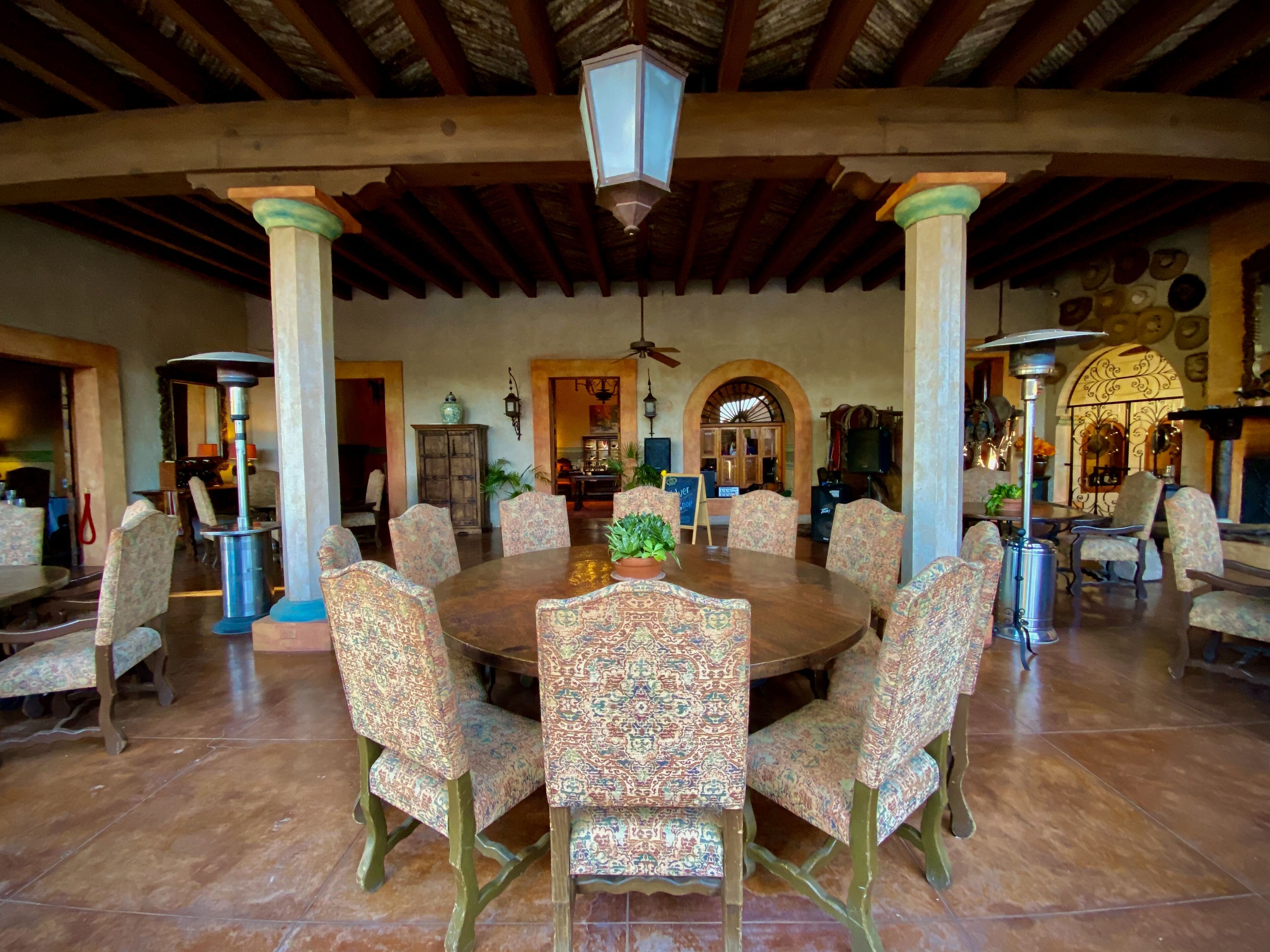 Un comedor espacioso con una gran mesa redonda rodeada de sillas con diseños, techo de madera y vista al área de la cocina.