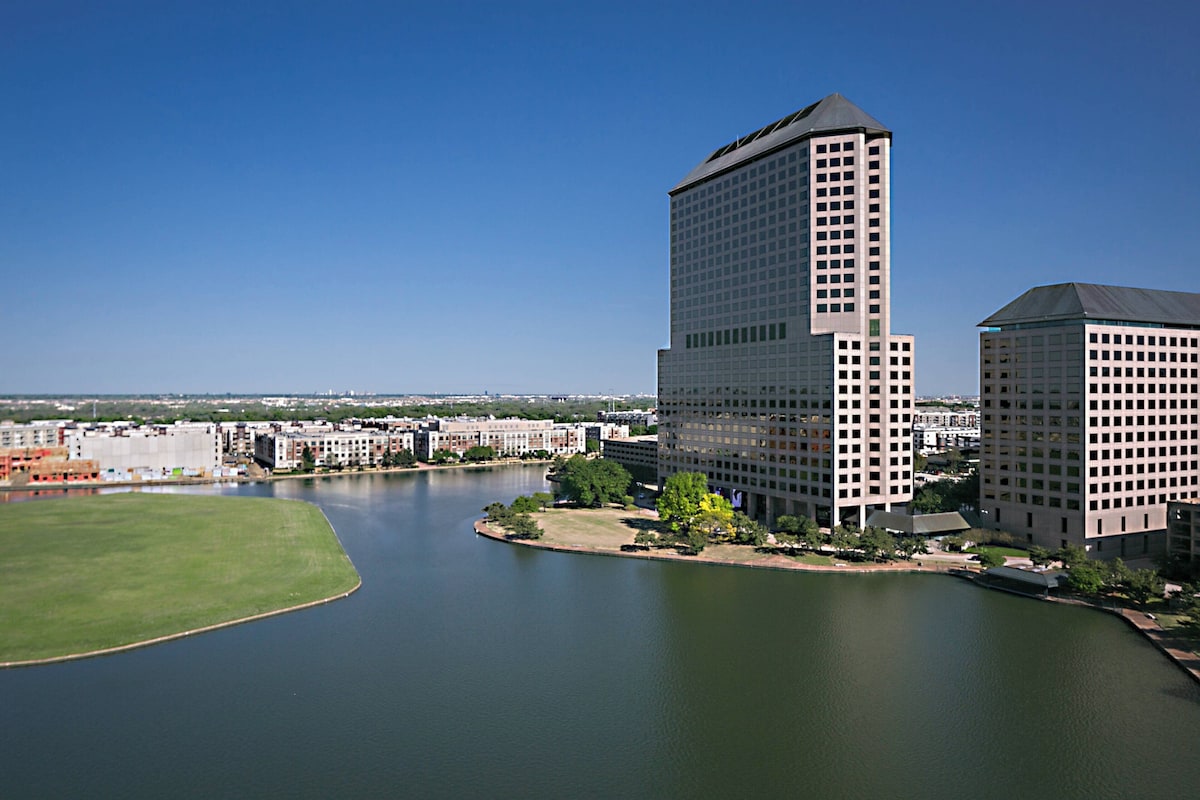 A high-rise building with a modern architectural design, situated next to a body of water, likely a river or lake, with a clear sky in the background.