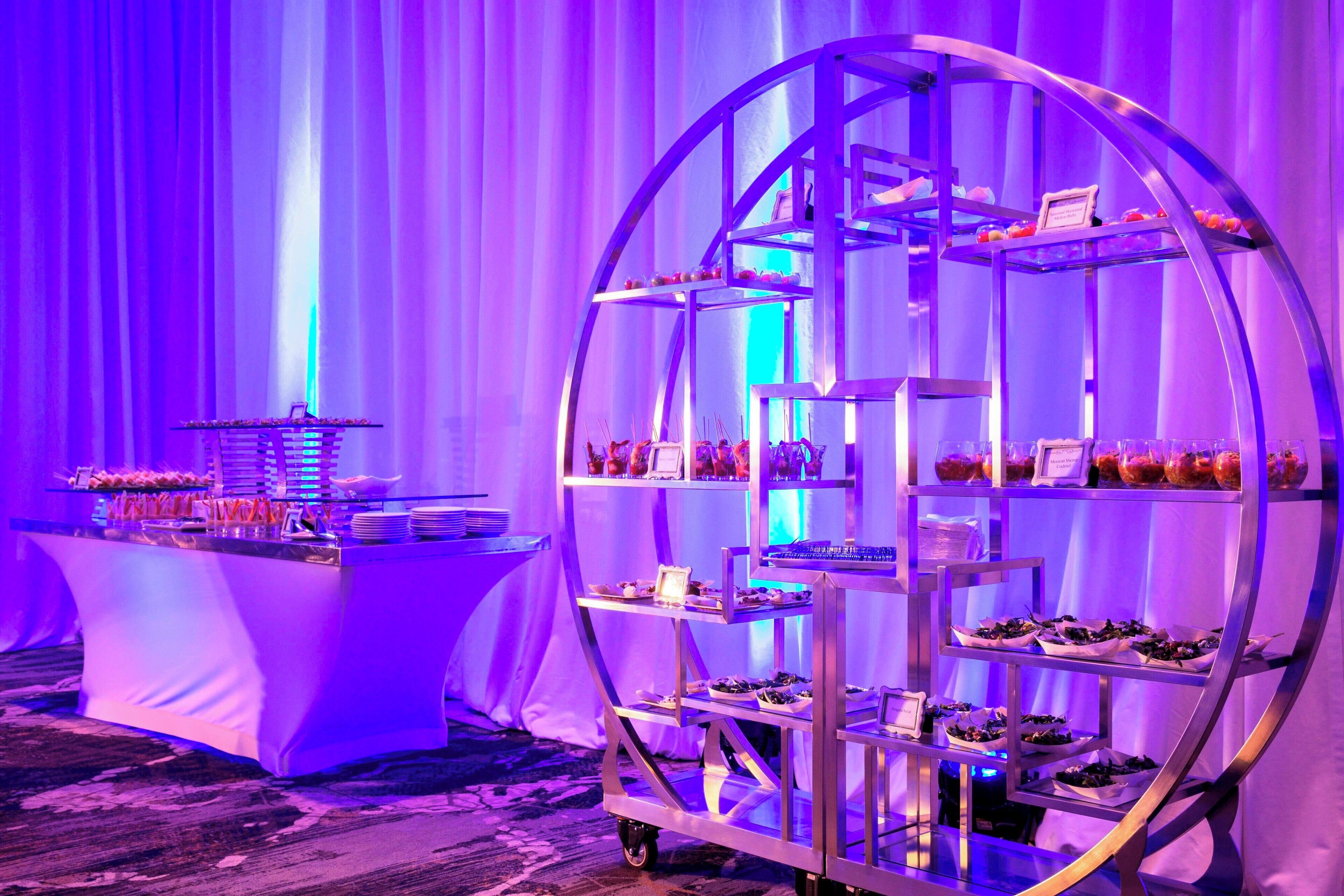 A buffet setup with multiple serving stations, including a central cart with tiered shelves and a side table with dishes.