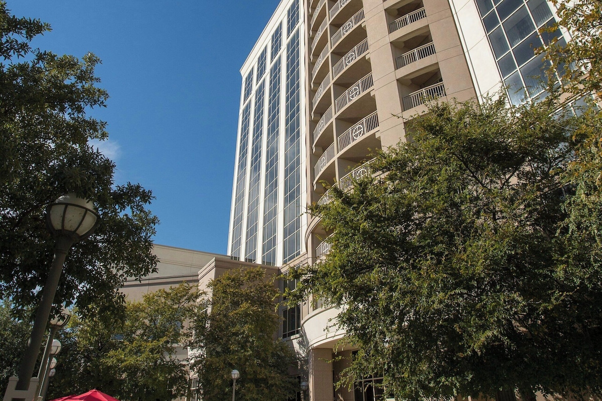A hotel courtyard with outdoor seating, a tall building with multiple balconies, and a clear blue sky.