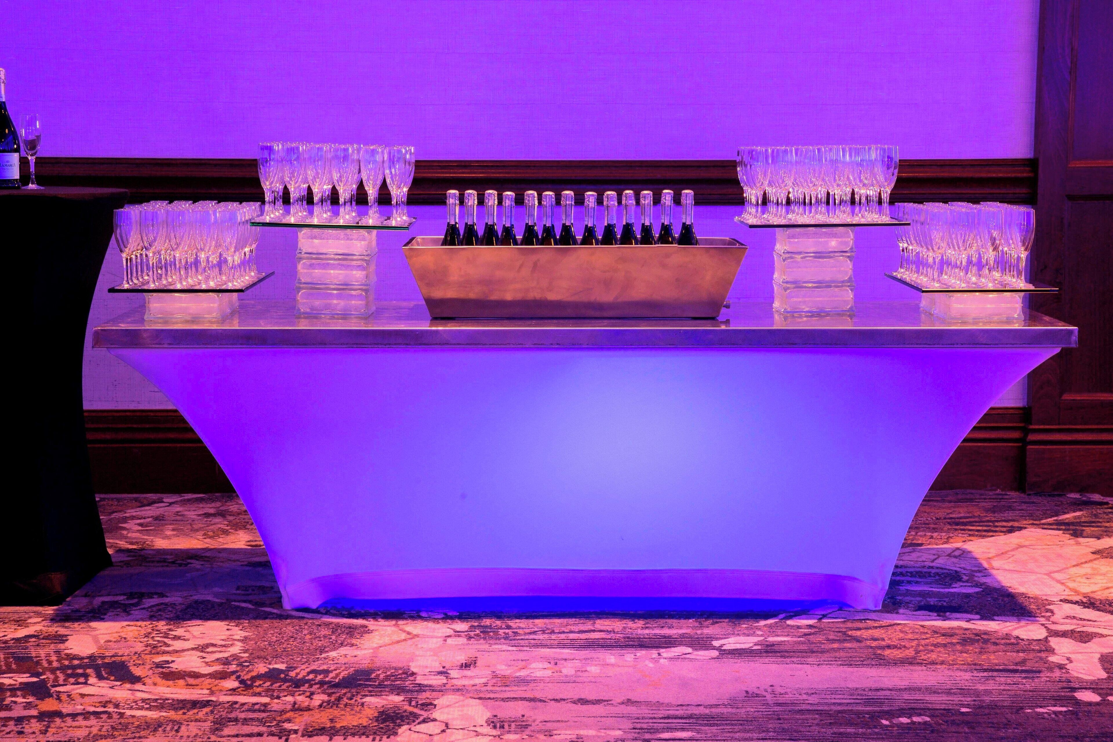 A bar area with a long counter, multiple wine bottles, and several glasses arranged on it.