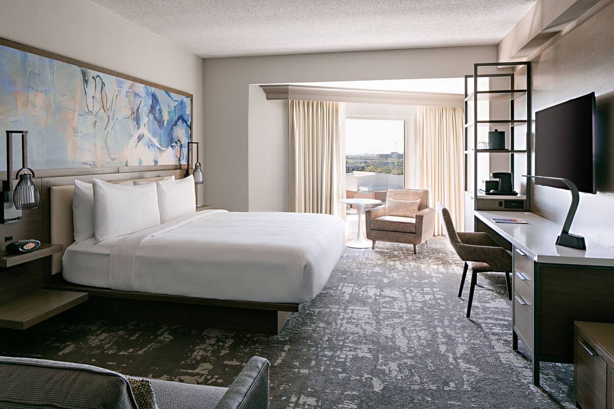 A hotel room with a large bed, a desk with a chair, a TV, and a painting on the wall.