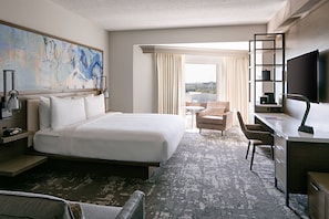 A hotel room with a large bed, a desk with a chair, a TV, and a painting on the wall.