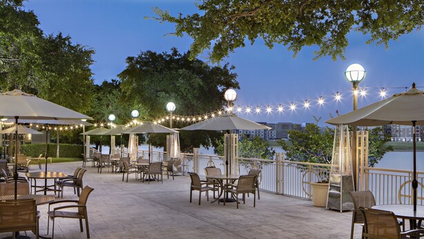 Un patio al aire libre con mesas, sillas, luces colgantes y sombrillas.
