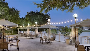 Une terrasse extérieure avec des tables et des chaises, des guirlandes lumineuses et des parasols.