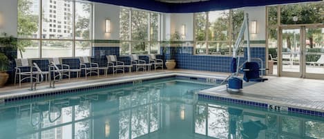 A pool area with chairs and a ladder, large windows, and a tiled floor.