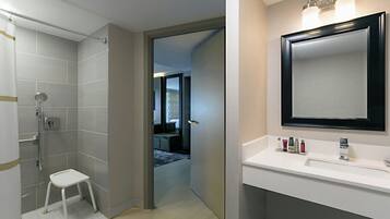 A modern bathroom with a shower, a small stool, and a vanity with a mirror and toiletries.